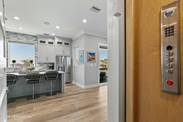 kitchen featuring a breakfast bar, stainless steel refrigerator with ice dispenser, glass insert cabinets, a healthy amount of sunlight, and white cabinets