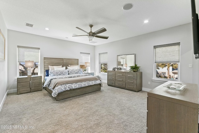 bedroom featuring ceiling fan, light colored carpet, multiple windows, and a textured ceiling