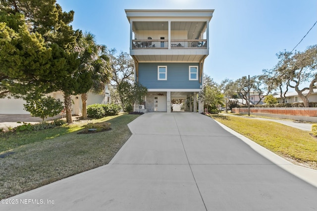 coastal home with a balcony, driveway, a carport, and a front yard