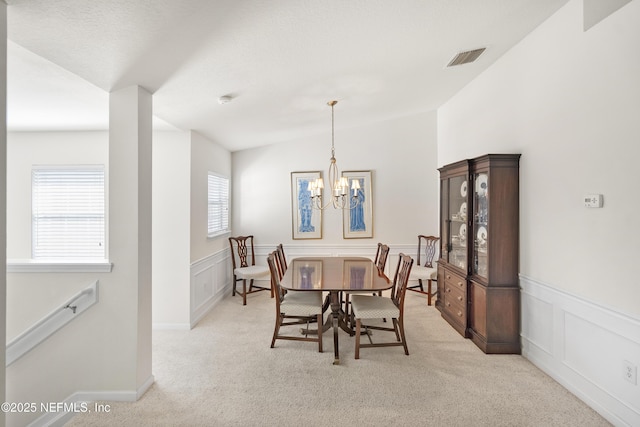 dining area with a notable chandelier, a wainscoted wall, visible vents, and light colored carpet