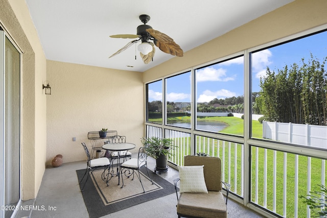 sunroom with ceiling fan and a water view