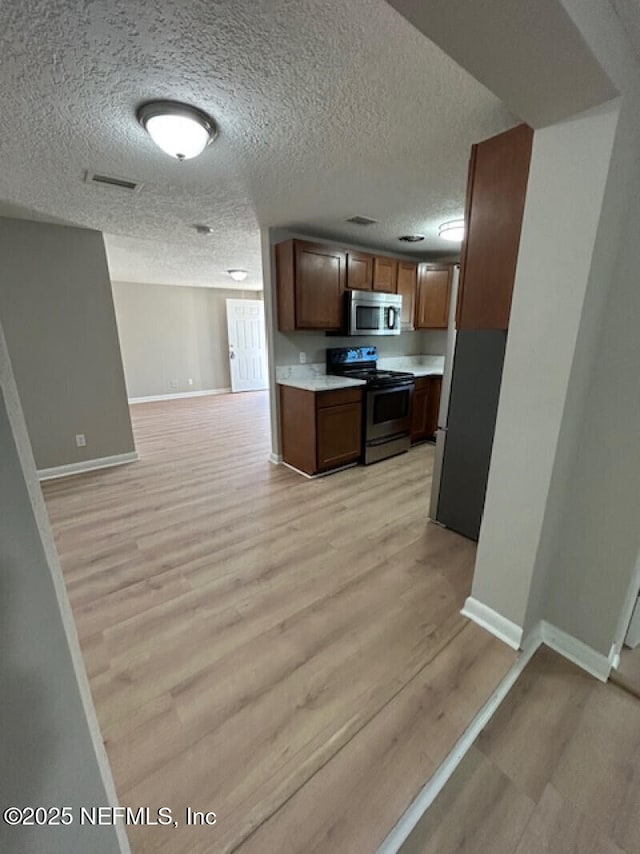 kitchen with a textured ceiling, stainless steel appliances, and light hardwood / wood-style flooring