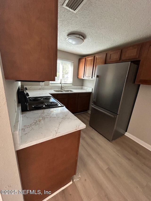 kitchen with sink, stainless steel fridge, light stone countertops, light hardwood / wood-style floors, and range