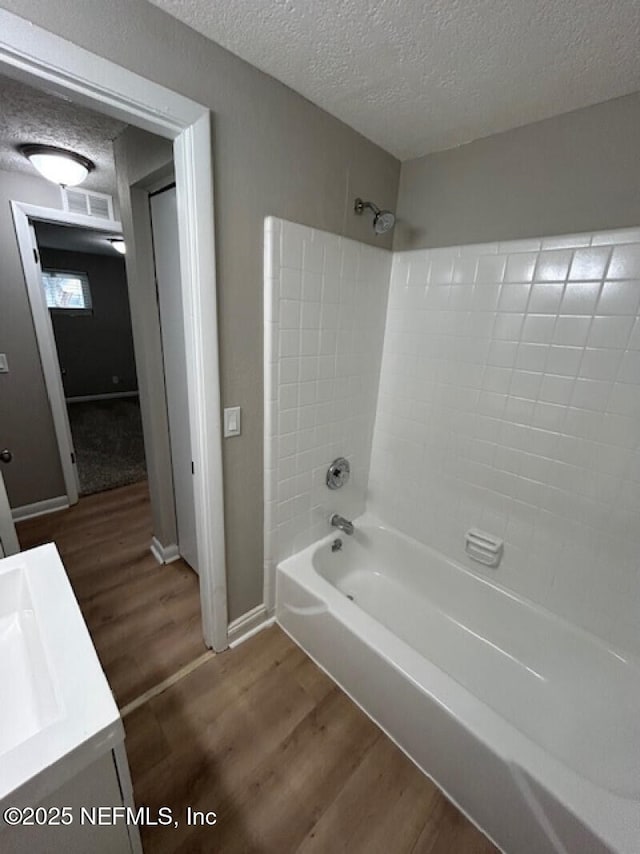 bathroom with hardwood / wood-style floors, tiled shower / bath combo, a textured ceiling, and vanity