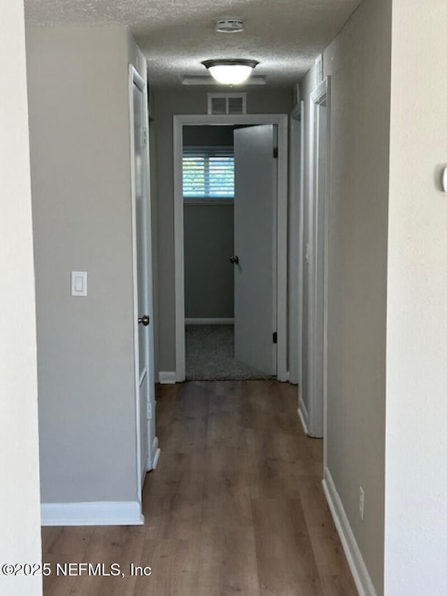 hallway with a textured ceiling and hardwood / wood-style flooring