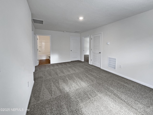 unfurnished bedroom featuring ensuite bath, dark carpet, and a textured ceiling