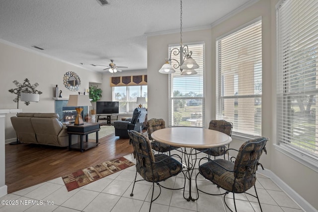 tiled dining area with a textured ceiling, plenty of natural light, ceiling fan with notable chandelier, and ornamental molding