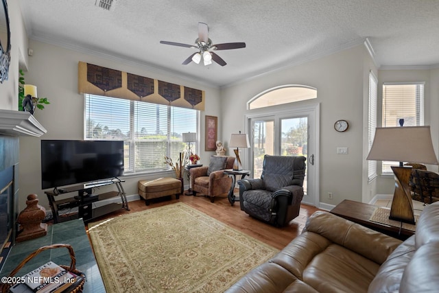 living room with hardwood / wood-style floors, crown molding, ceiling fan, a textured ceiling, and a fireplace