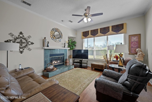 living room featuring a tile fireplace, crown molding, ceiling fan, a textured ceiling, and wood-type flooring