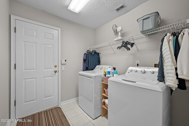 laundry room featuring washing machine and clothes dryer, light tile patterned floors, and a textured ceiling