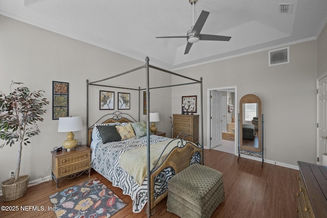 bedroom featuring hardwood / wood-style floors, ensuite bathroom, ceiling fan, a textured ceiling, and a tray ceiling