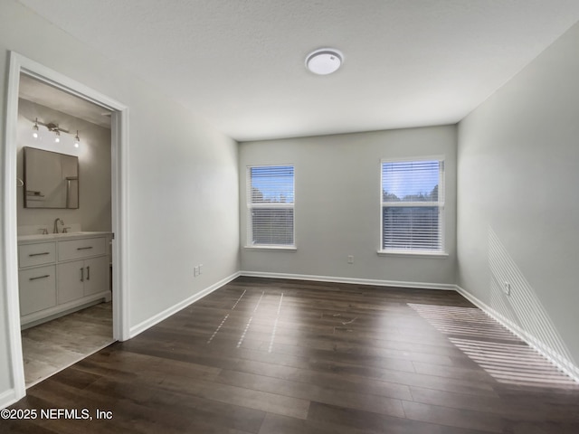 unfurnished bedroom featuring ensuite bath, dark wood-type flooring, and sink