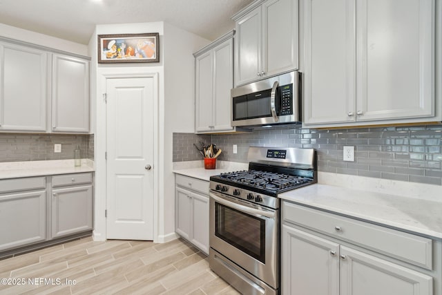 kitchen featuring appliances with stainless steel finishes, light stone countertops, decorative backsplash, and gray cabinetry