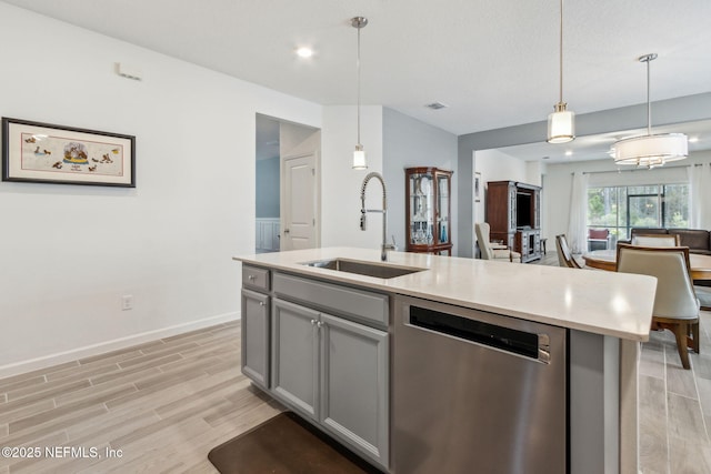 kitchen featuring sink, decorative light fixtures, gray cabinets, dishwasher, and a kitchen island with sink