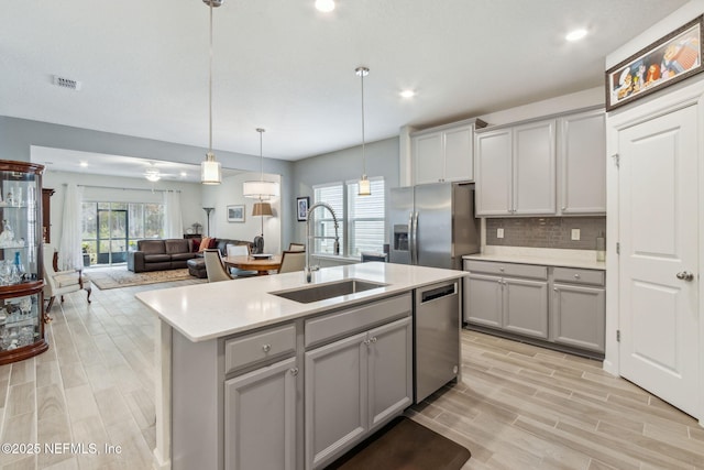 kitchen with stainless steel appliances, sink, a kitchen island with sink, and gray cabinets