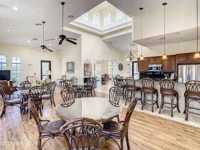 dining area with ceiling fan, light wood-type flooring, and a high ceiling