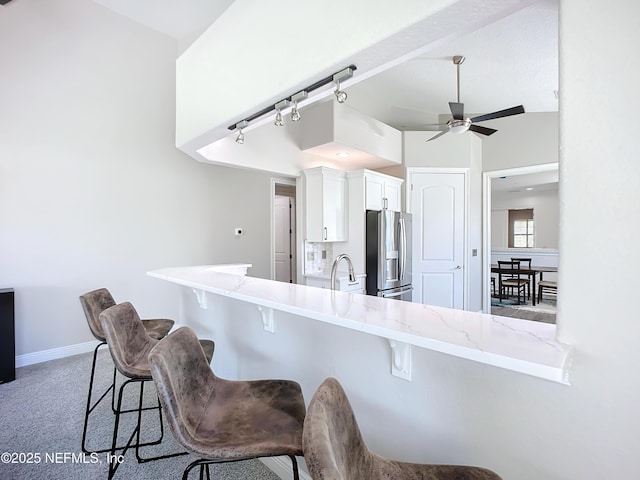 kitchen with stainless steel refrigerator with ice dispenser, a breakfast bar area, white cabinetry, kitchen peninsula, and ceiling fan