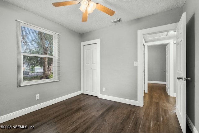 unfurnished bedroom with a textured ceiling, dark wood-type flooring, a closet, and ceiling fan