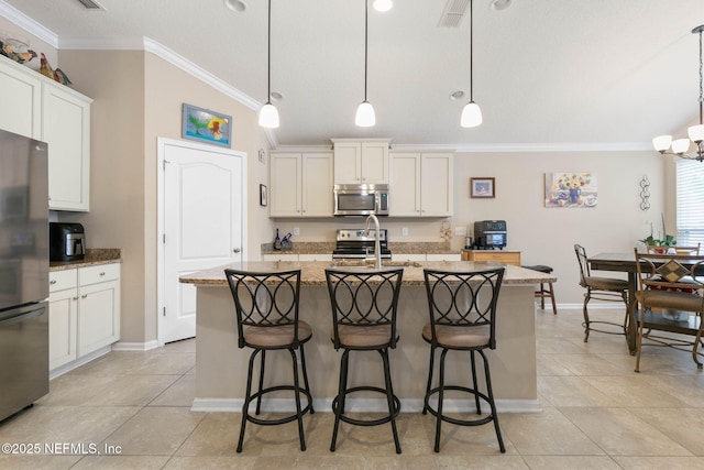 kitchen with light stone countertops, hanging light fixtures, stainless steel appliances, a kitchen island with sink, and white cabinets