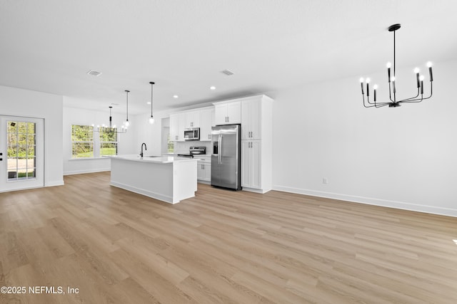 kitchen featuring white cabinets, a center island with sink, light hardwood / wood-style flooring, appliances with stainless steel finishes, and decorative light fixtures