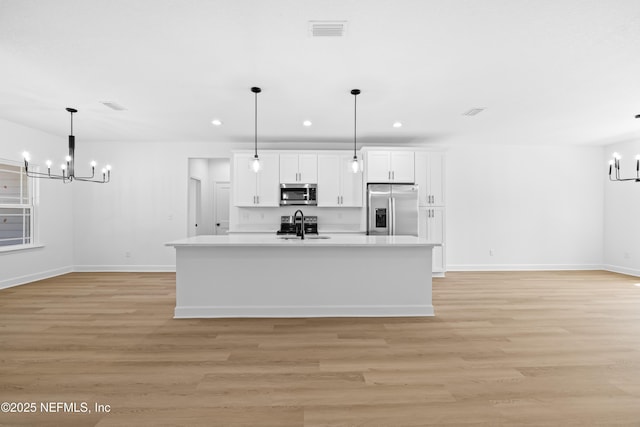 kitchen with hanging light fixtures, stainless steel appliances, a chandelier, white cabinets, and light wood-type flooring