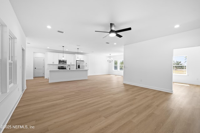 unfurnished living room featuring light hardwood / wood-style flooring, ceiling fan with notable chandelier, and sink