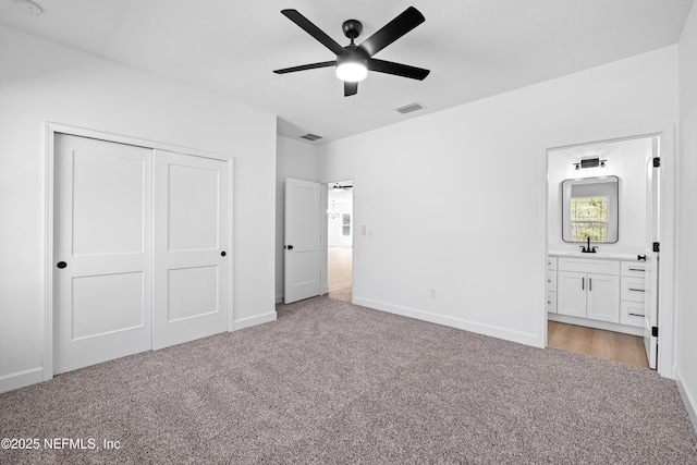 unfurnished bedroom with ceiling fan, sink, ensuite bathroom, light colored carpet, and a closet