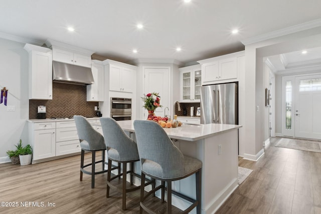 kitchen with appliances with stainless steel finishes, a kitchen breakfast bar, a center island with sink, light hardwood / wood-style floors, and white cabinetry