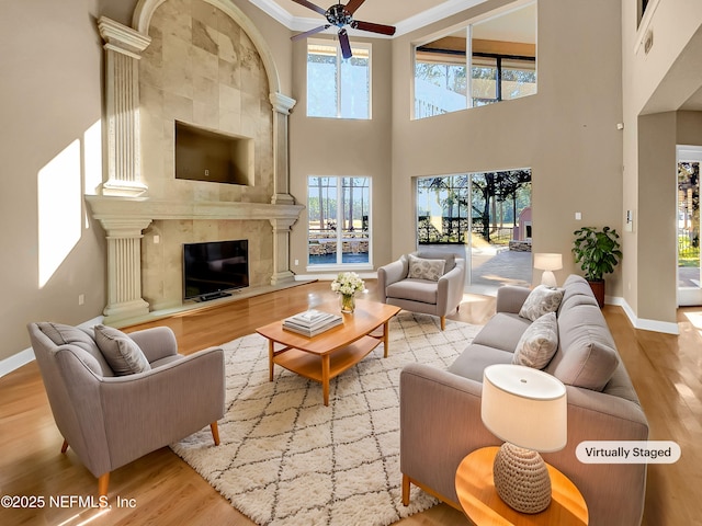 living room with ceiling fan, light wood-type flooring, ornamental molding, and a high ceiling