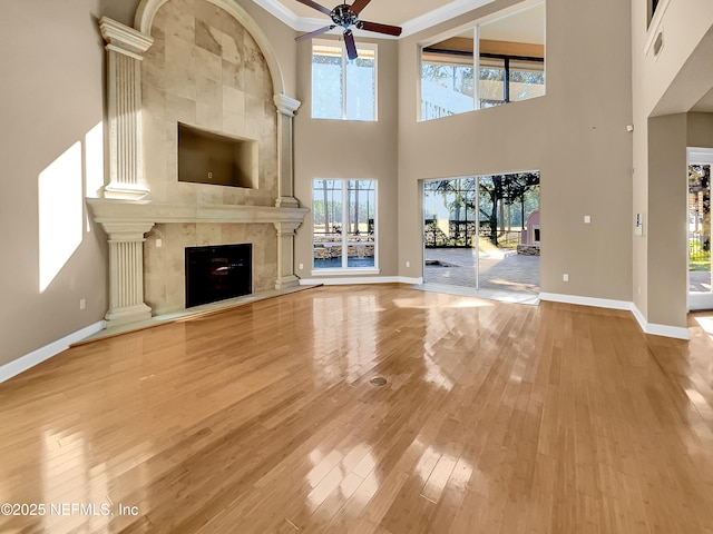 unfurnished living room featuring ceiling fan, crown molding, hardwood / wood-style floors, a towering ceiling, and a fireplace