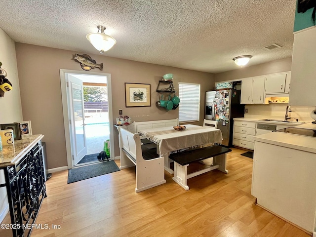 kitchen featuring white cabinetry, sink, stainless steel refrigerator with ice dispenser, light hardwood / wood-style floors, and a textured ceiling