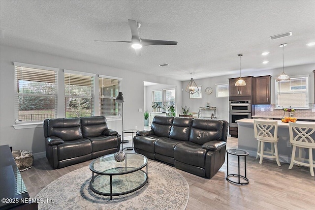 living room featuring ceiling fan with notable chandelier, a textured ceiling, and light hardwood / wood-style flooring