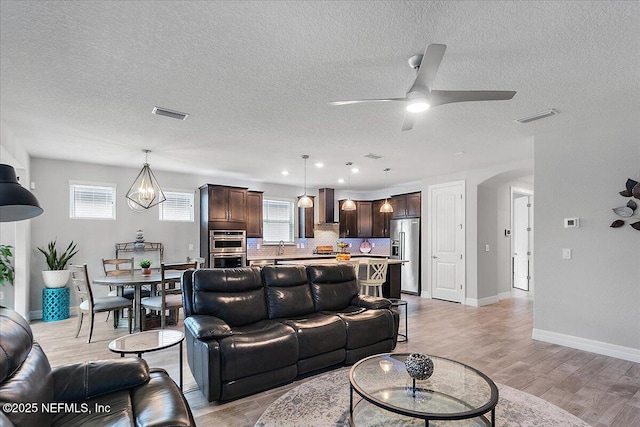 living room with ceiling fan with notable chandelier, sink, a textured ceiling, and light wood-type flooring