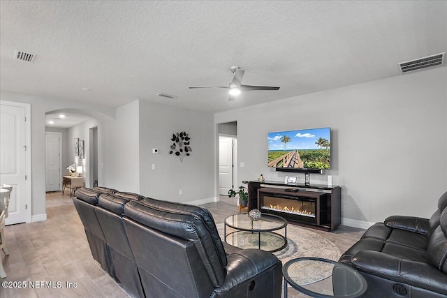 living room with ceiling fan, a textured ceiling, and light hardwood / wood-style flooring