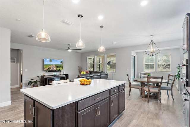 kitchen with light hardwood / wood-style floors, dark brown cabinets, a kitchen island, pendant lighting, and ceiling fan with notable chandelier