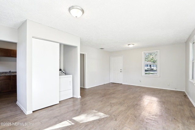 unfurnished living room with a textured ceiling, light wood-type flooring, and washer / clothes dryer