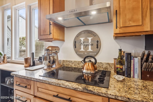 kitchen with light stone countertops, a wealth of natural light, black electric stovetop, and extractor fan