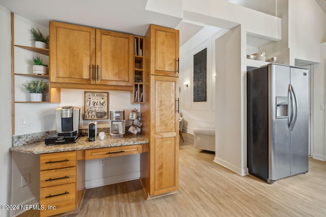 kitchen featuring light wood-type flooring, stainless steel fridge with ice dispenser, built in desk, and light stone counters