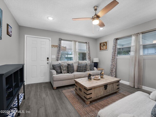 living room featuring ceiling fan, a textured ceiling, a wealth of natural light, and dark wood-type flooring