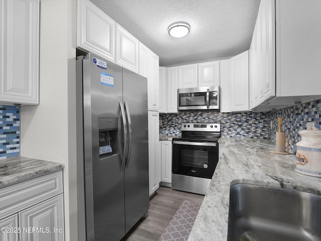 kitchen featuring light stone countertops, stainless steel appliances, tasteful backsplash, a textured ceiling, and white cabinets