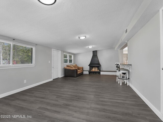 unfurnished room with a wood stove, dark wood-type flooring, and a textured ceiling