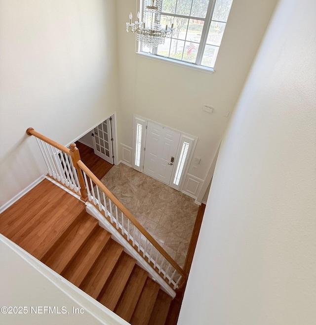 foyer entrance featuring baseboards, stairway, a towering ceiling, wood finished floors, and a notable chandelier