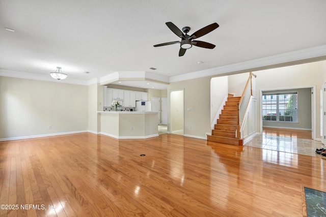 unfurnished living room featuring ornamental molding, a ceiling fan, light wood-style floors, baseboards, and stairs