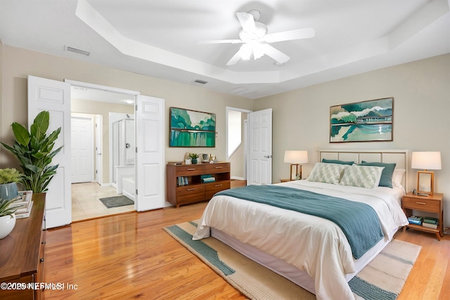 bedroom with visible vents, a raised ceiling, baseboards, and light wood-style flooring