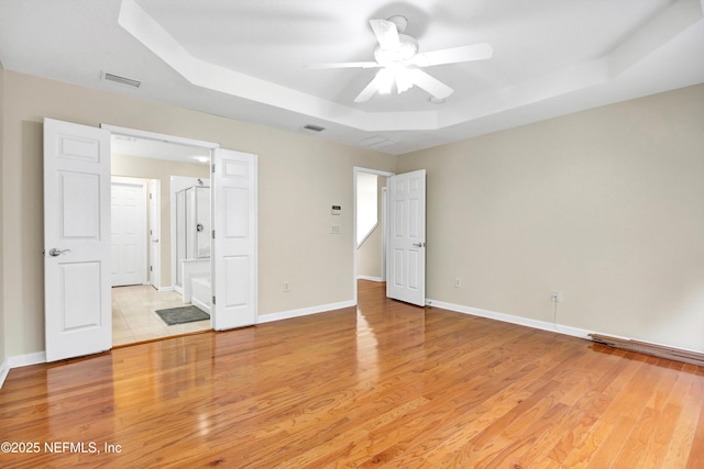 empty room with a tray ceiling, light wood-style floors, visible vents, and baseboards