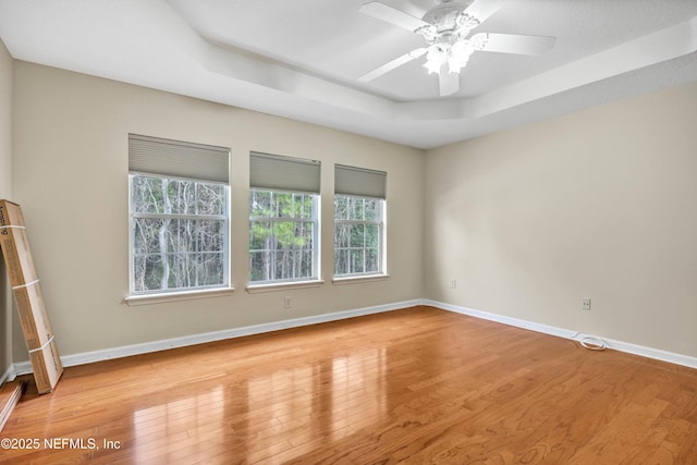 spare room featuring baseboards, light wood-style floors, a tray ceiling, and a ceiling fan