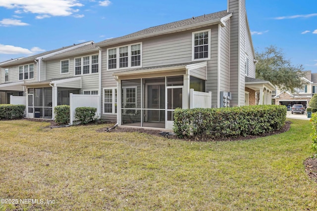 rear view of property featuring a chimney, a yard, and a sunroom