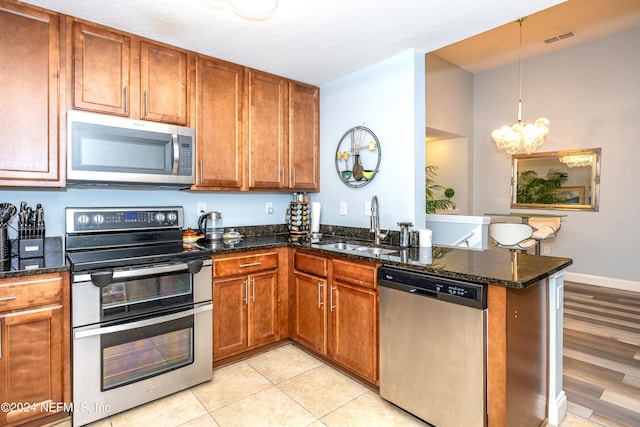 kitchen featuring stainless steel appliances, sink, decorative light fixtures, dark stone countertops, and a chandelier