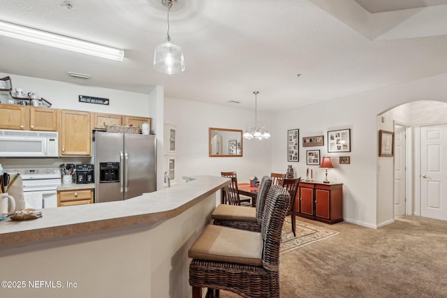 kitchen featuring white appliances, hanging light fixtures, a kitchen breakfast bar, light carpet, and light brown cabinets