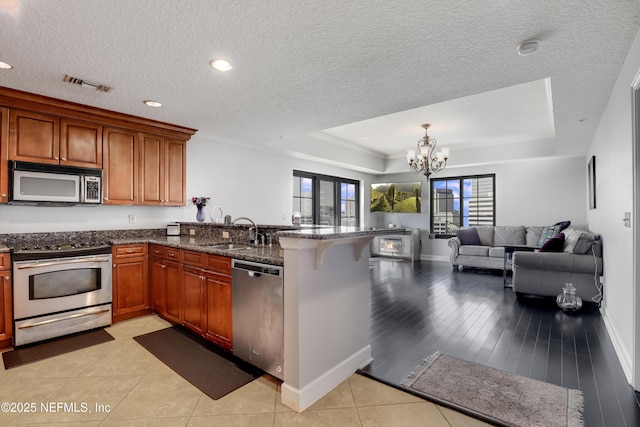 kitchen featuring stainless steel appliances, a raised ceiling, a notable chandelier, and kitchen peninsula